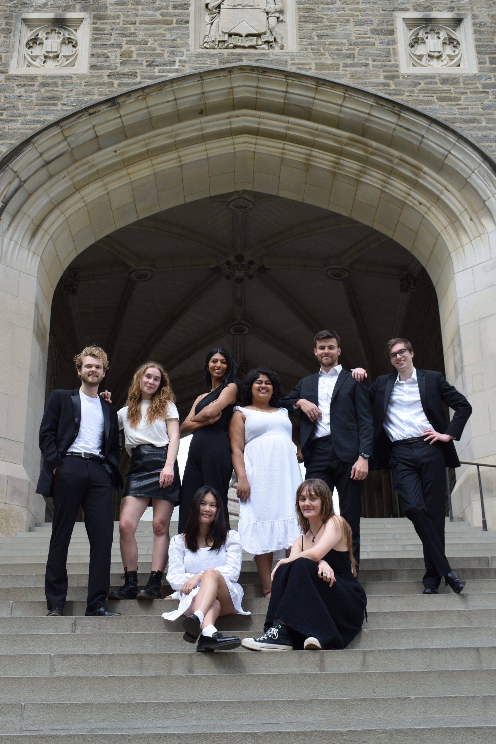 Student vocalists standing and smiling under a concrete arch on campus