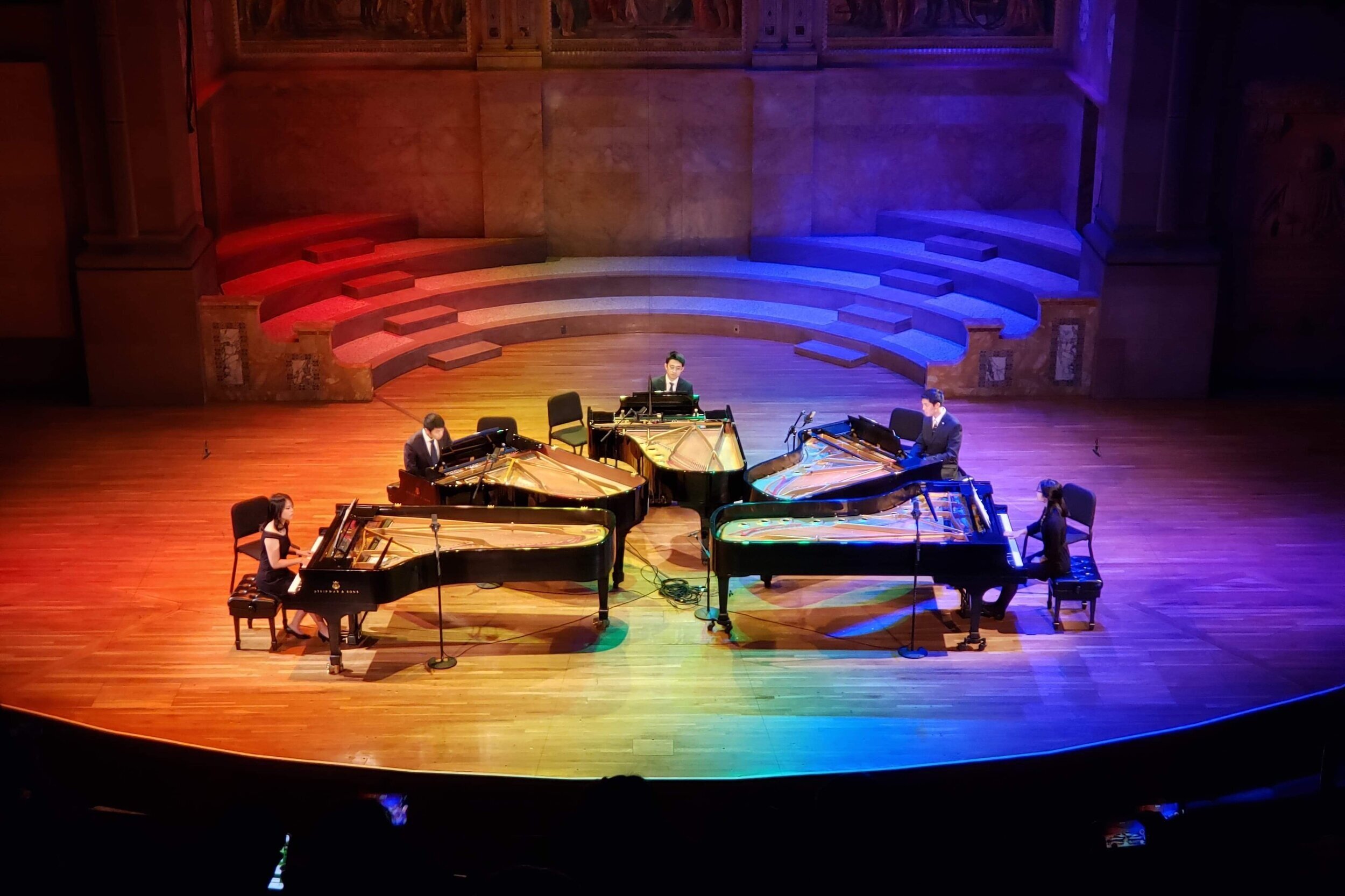 5 large pianos on stage at the same time, with pianists performing