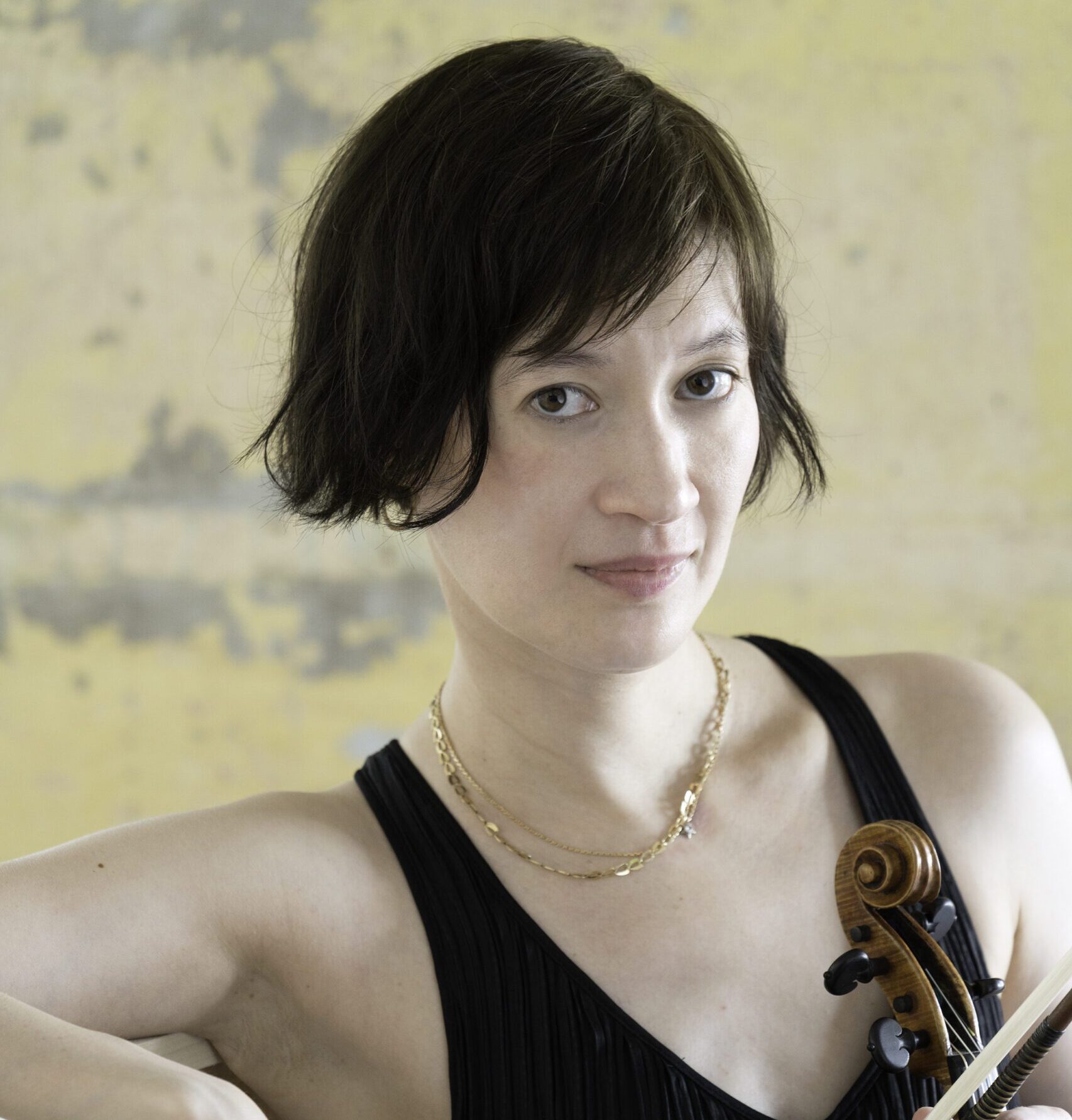 headshot of Miranda Cuckson, who is holding her violin in front of a beige background