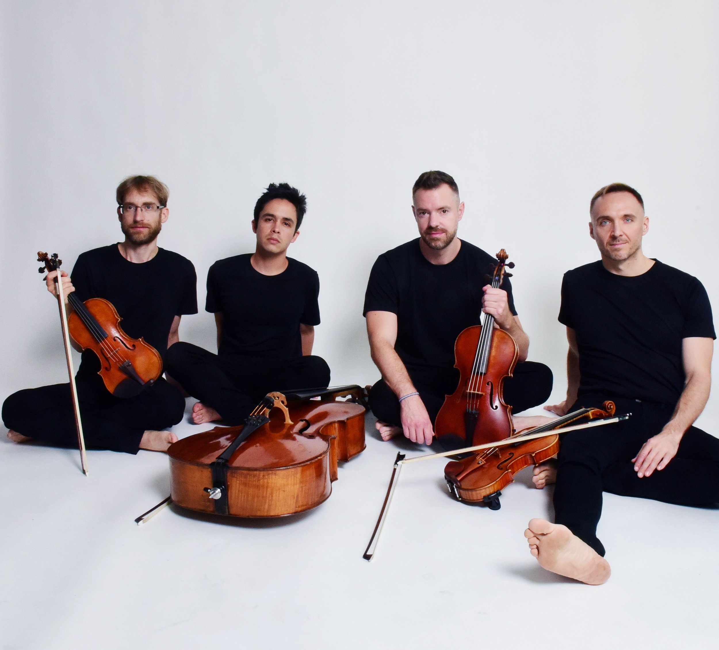 A group of string musicians sitting down near a white background