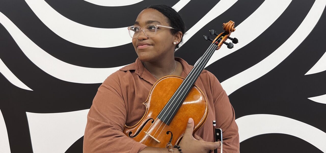 A person holding a viola in front of a black and white background