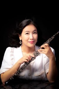 A person wearing a white shirt and holding an oboe